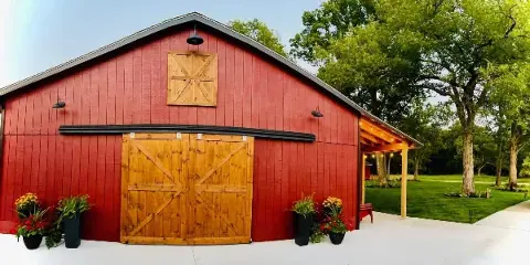 Exterior view of a red wooden barn venue with a covered patio and potted flowers.