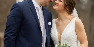A bride and groom standing together outdoors, with the bride holding a bouquet of white and pink roses with eucalyptus.