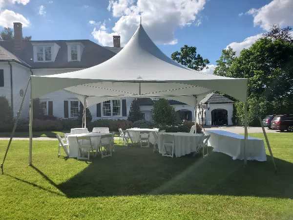 A white event tent set up on a grassy lawn with white round tables and chairs arranged underneath.