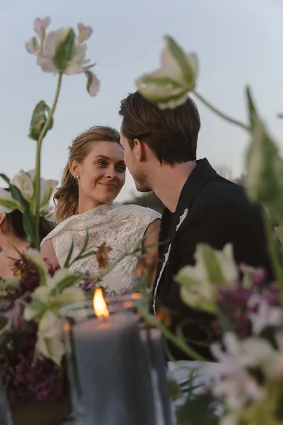 Bride and groom sharing an intimate moment at a wedding reception table with floral arrangements and a lit candle.