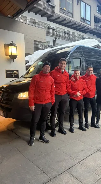 Eagle Mountain Express chauffeurs in red jackets standing next to a black Mercedes-Benz Sprinter van at a Vail Valley resort in winter.