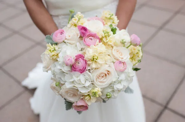 Bride in a white wedding dress holding a round bouquet of white and pink roses, ranunculus, and hydrangeas.
