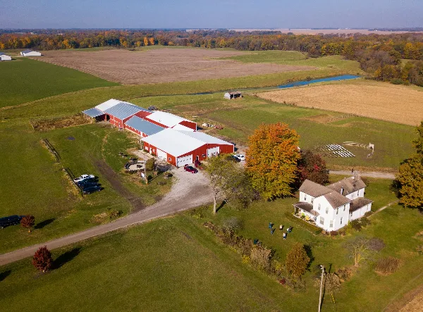 Aerial view of a red barn wedding venue and white farmhouse on a 10-acre farm with green fields and outdoor seating.