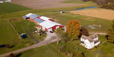 Aerial view of a red barn wedding venue and white farmhouse on a 10-acre farm with green fields and outdoor seating.