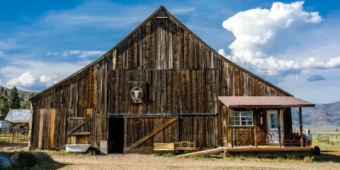 Exterior view of a rustic wooden barn venue with a small attached porch and a blue sky background.