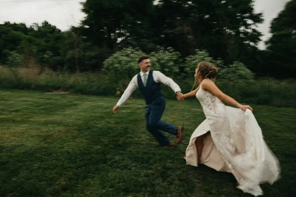 A bride and groom dancing on a grassy lawn surrounded by trees and greenery.