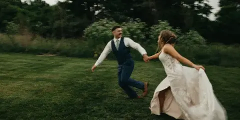 A bride and groom dancing on a grassy lawn surrounded by trees and greenery.