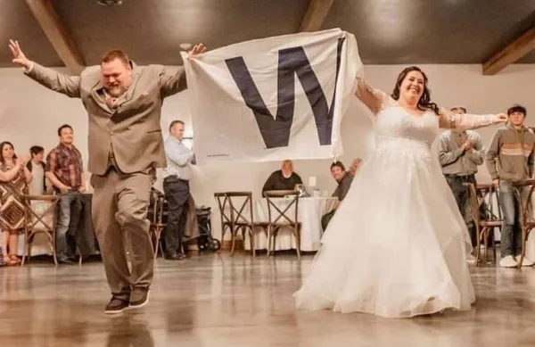 A bride and groom dancing in a wedding reception hall, holding up a banner with the letter 'W'.
