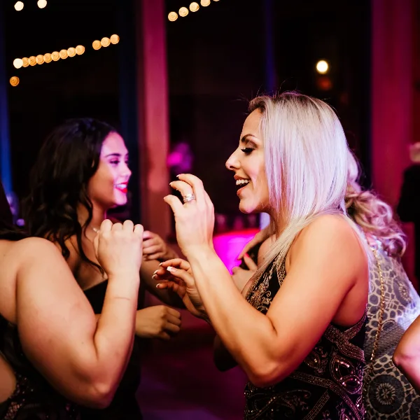 Guests dancing at a wedding reception under pink and purple lighting.