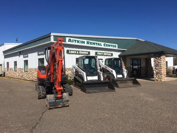 Exterior view of the Aitkin Rental Center building with construction equipment parked in front.
