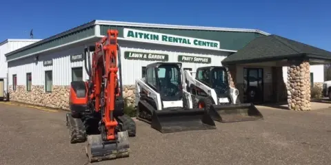 Exterior view of the Aitkin Rental Center building with construction equipment parked in front.