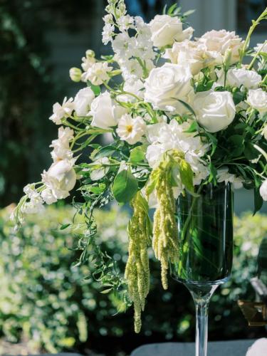 A close-up of a white rose and greenery floral arrangement in a tall glass vase.