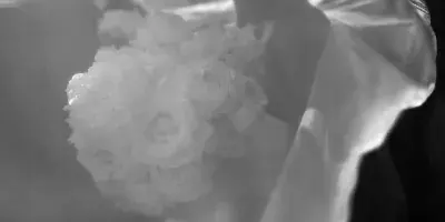 Black and white photograph of a bride and groom kissing under a veil with a bouquet of white roses.