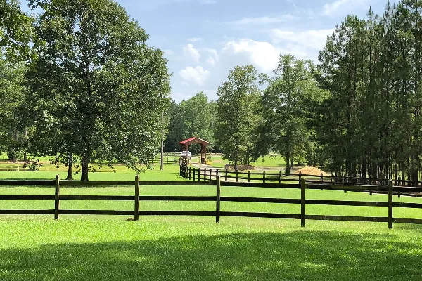 A view of a grassy field with a wooden fence and a covered bridge in the distance.