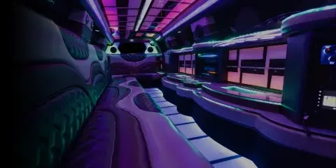 Interior view of a luxury party bus with purple and green LED lighting and plush seating.