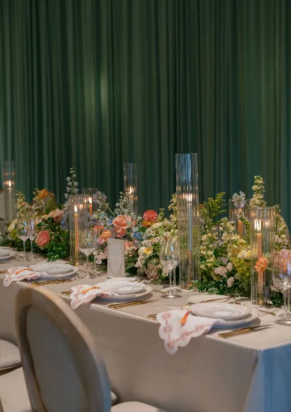 A close-up of an elegant wedding table setting with white linens, gold flatware, glassware, and floral centerpieces.