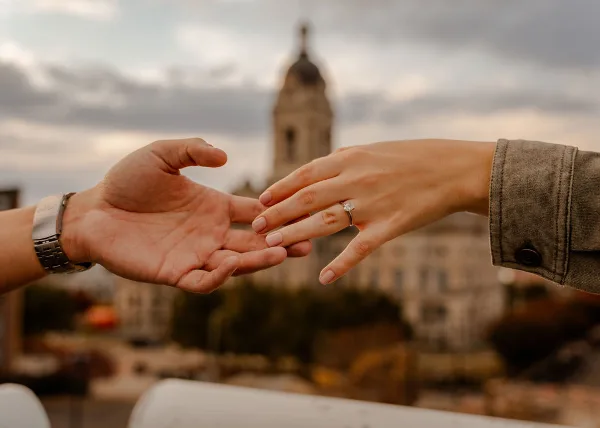 A close-up of two hands exchanging a diamond ring with the Old Courthouse tower in the background.