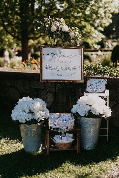 A wedding welcome sign for Emily and Michael decorated with a floral garland and flanked by buckets of white hydrangeas.