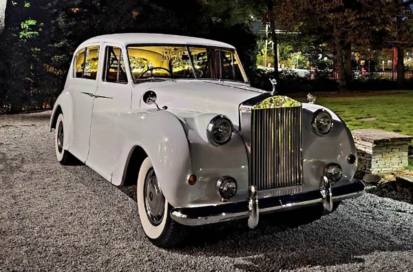 A vintage white Rolls-Royce luxury car parked outdoors at night.