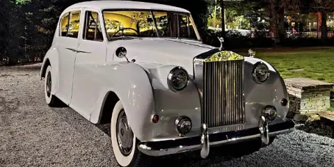 A vintage white Rolls-Royce luxury car parked outdoors at night.