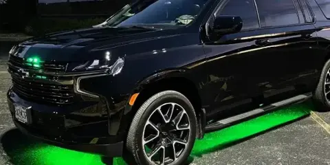 A black Chevrolet SUV parked in a lot with green underglow lighting.