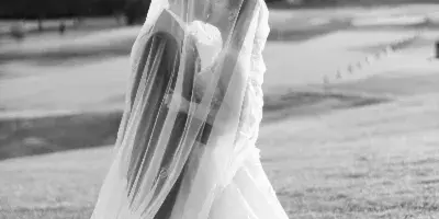 Black and white photo of a bride and groom kissing under a veil on a grassy field.