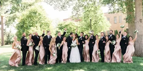 A wedding party posing outdoors on a lawn with the bride and groom in the center.