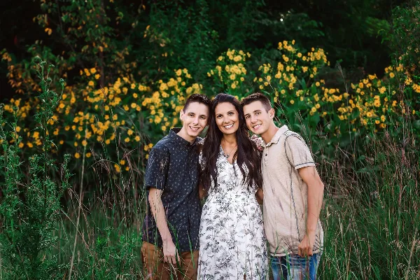 A professional outdoor portrait of a mother and two sons standing together in a field of yellow flowers.