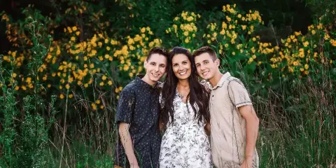 A professional outdoor portrait of a mother and two sons standing together in a field of yellow flowers.