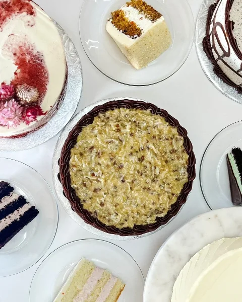 An overhead view of several cakes and pastries, including a decorated cake with flowers, a slice of layered cake, and a chocolate-topped dessert.