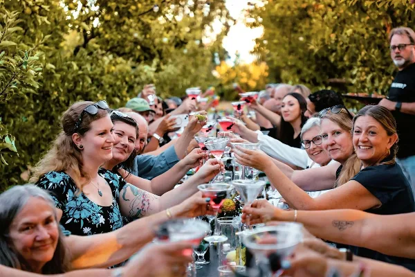 A group of smiling guests at an outdoor event raising cocktail glasses in a toast.