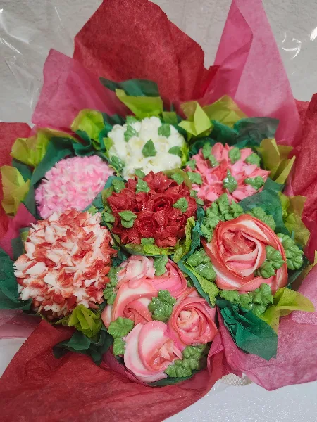 A bouquet of decorated cupcakes in various colors and styles, arranged with green leaves and red paper.