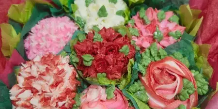 A bouquet of decorated cupcakes in various colors and styles, arranged with green leaves and red paper.
