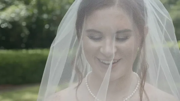 Cinematic close-up of a smiling bride wearing a veil and pearl necklace.