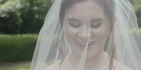 Cinematic close-up of a smiling bride wearing a veil and pearl necklace.