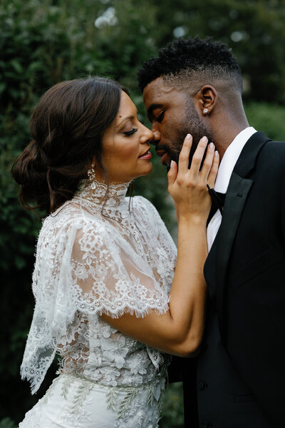 A bride in a lace gown and a groom in a tuxedo share an intimate moment outdoors.