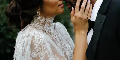 A bride in a lace gown and a groom in a tuxedo share an intimate moment outdoors.