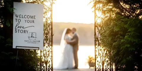A wedding couple embracing in the background with a 'Welcome to Your Love Story' sign featuring the Hariel Xavier Photography logo in the foreground.