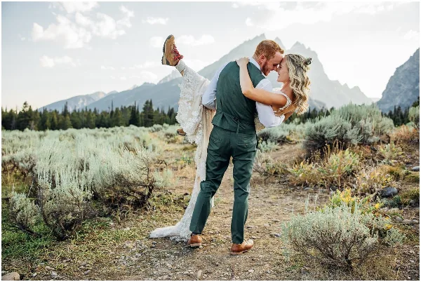A bride and groom in a dip pose with a mountain range in the background.