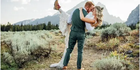 A bride and groom in a dip pose with a mountain range in the background.