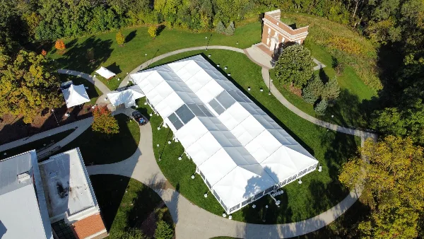 Aerial view of a large white event tent installed on a grassy lawn near a building.