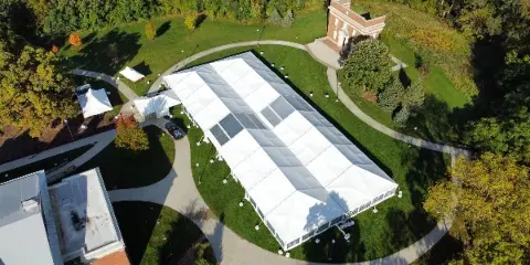 Aerial view of a large white event tent installed on a grassy lawn near a building.