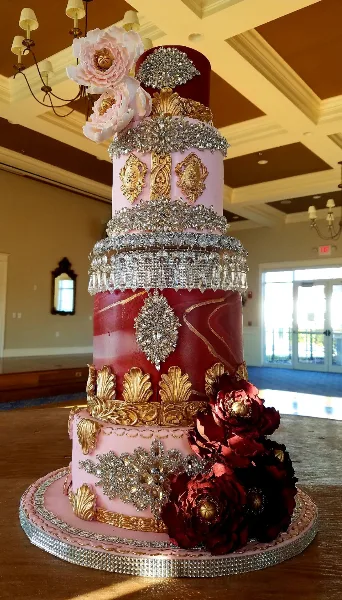 Ornate multi-tier pink and burgundy wedding cake decorated with gold and crystal details.
