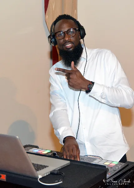 A professional DJ wearing headphones and a white shirt operating a mixing console and laptop.