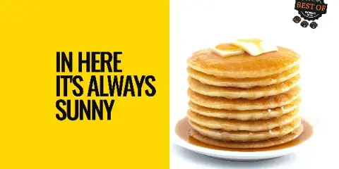 A tall stack of pancakes topped with butter and syrup on a white plate.