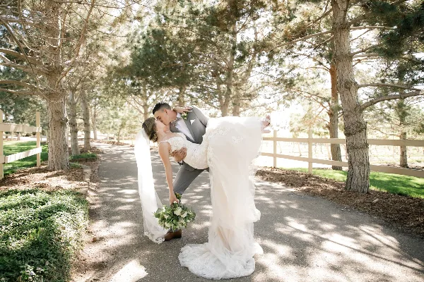 Bride and groom kissing on a tree-lined outdoor path at a wedding venue