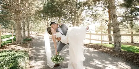 Bride and groom kissing on a tree-lined outdoor path at a wedding venue