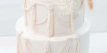 A two-tier white wedding cake decorated with elaborate fondant tassels and dried floral accents.