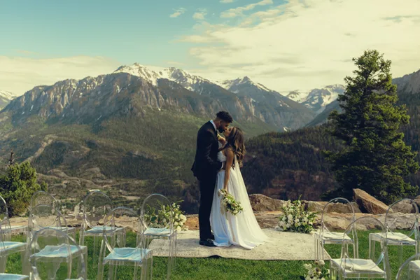 A bride and groom sharing a moment at an outdoor wedding ceremony with a backdrop of snow-capped mountains.