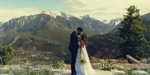 A bride and groom sharing a moment at an outdoor wedding ceremony with a backdrop of snow-capped mountains.